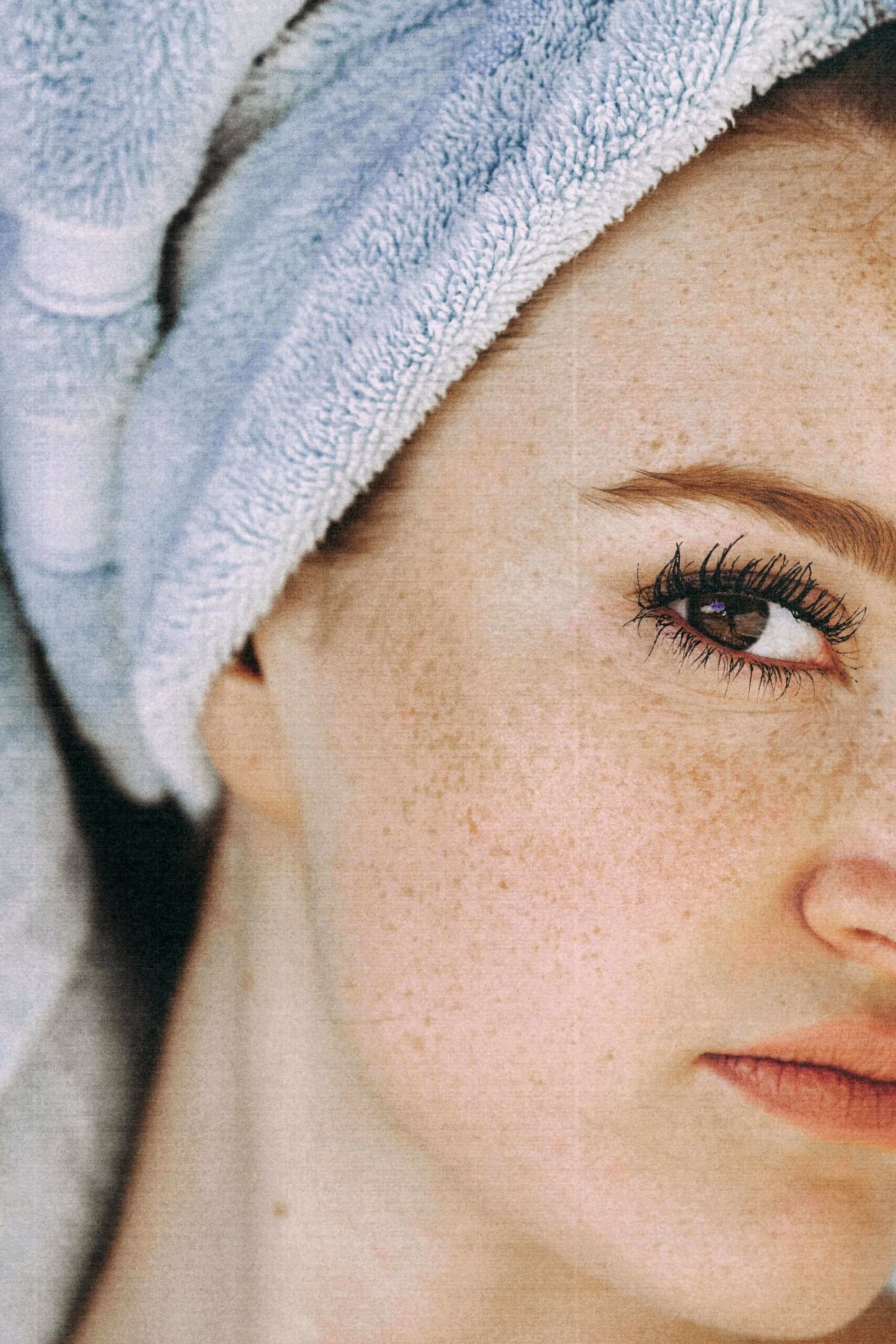 Close up of womans face, it is cropped showing the right side of her face, she has a blue towel wrapped around her hair